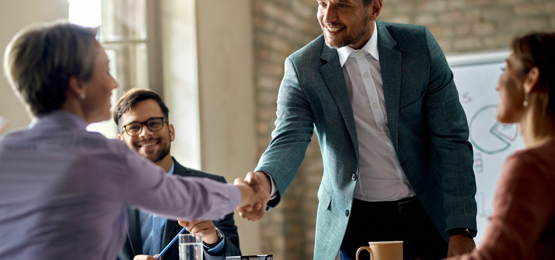 Business coworkers shaking hands during a meeting in the office. Focus is on a businessman.